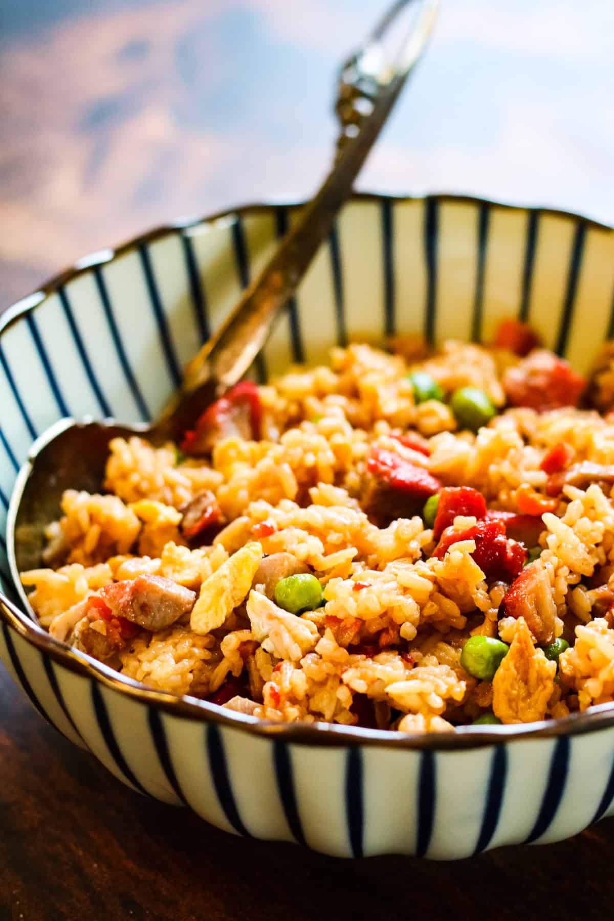 fried rice in a blue-and-white striped bowl on a wooden tableThe photo is shot from a low angle.
