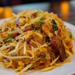 square photo of singapore rice noodles on a white plate shot from a low angle