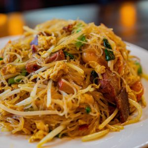 square photo of singapore rice noodles on a white plate shot from a low angle