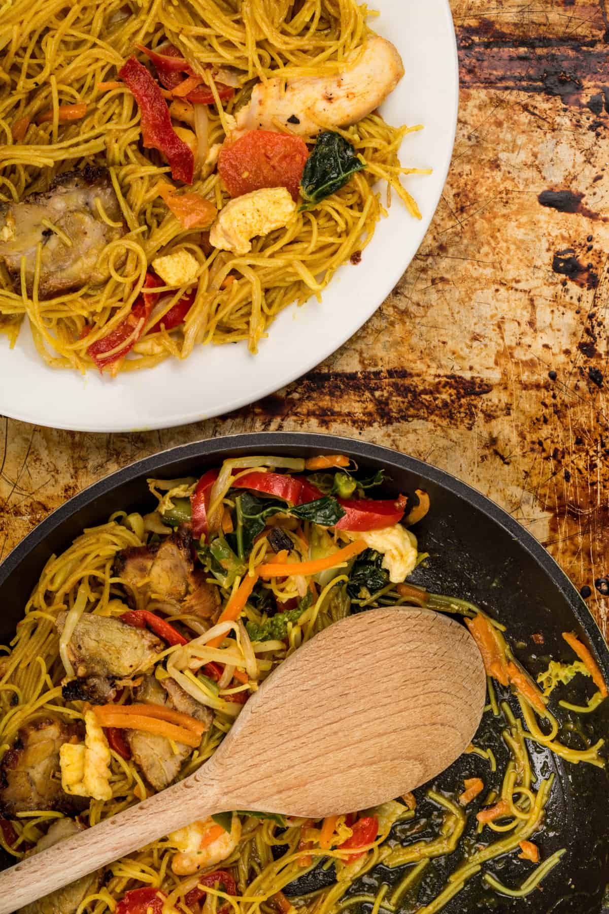 overhead shot of a skillet with Singapore noodles and a plate of Singapore noodles next to it.