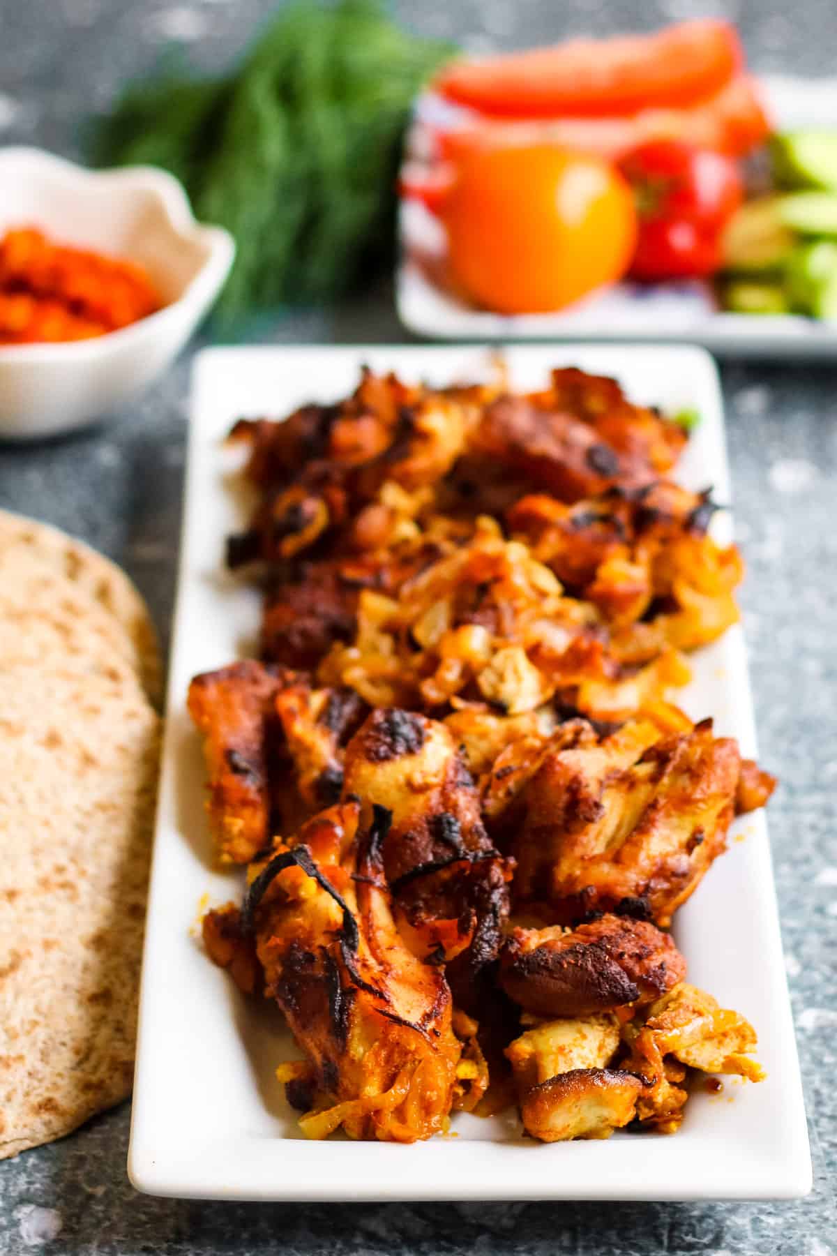 Chicken kebabs on a white plate with vegetables; chicken shwarma recipe.