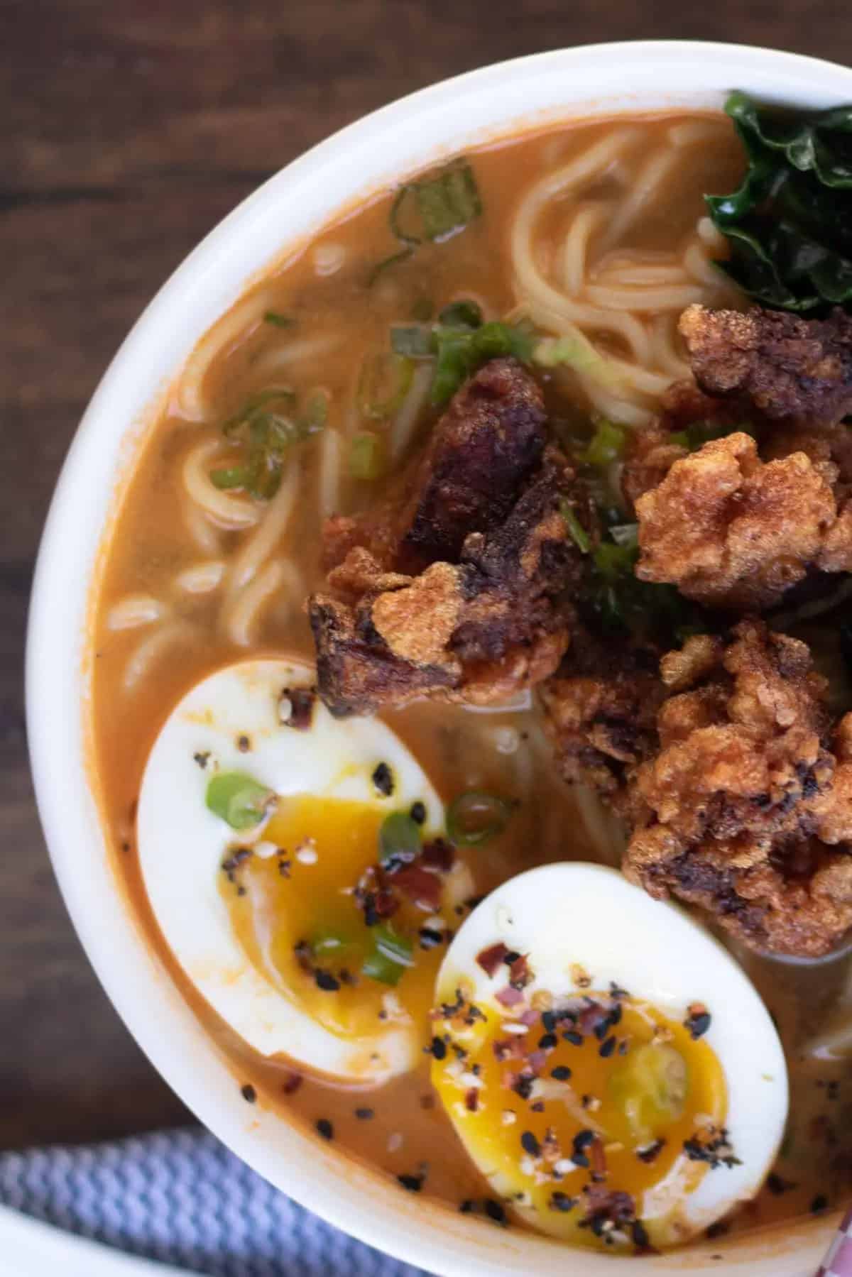 Bowl of miso ramen with broth, noodles, fried chicken pieces, soft-boiled eggs, green onions, and seasonings, viewed from above.