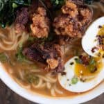Closeup overhead shot of a bowl of spicy miso ramen topped with chicken karaage, or Japanese fried chicken, soft boiled egg, and sauteed kale.