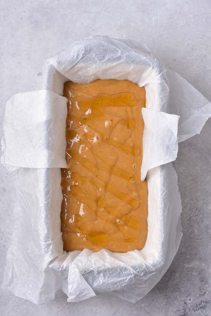 A loaf tin lined with parchment paper, filled with light brown honey cake batter, ready for baking.