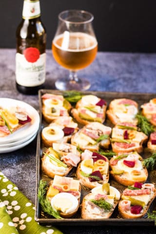 A tray of chlebicky appetizers on a table next to a bottle of beer.