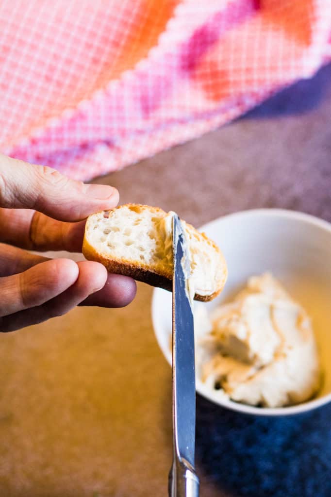 A shot of a person spreading anchovy butter onto a slice of bread.