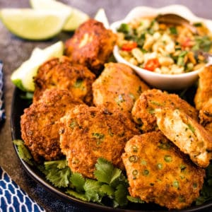 low angle shot of fish cakes on a plate with dipping sauce and limes in the background