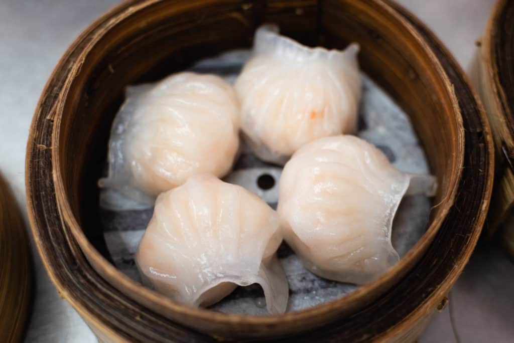 low angle shot of 4 har gow shrimp dumplings in a bamboo steamer basket