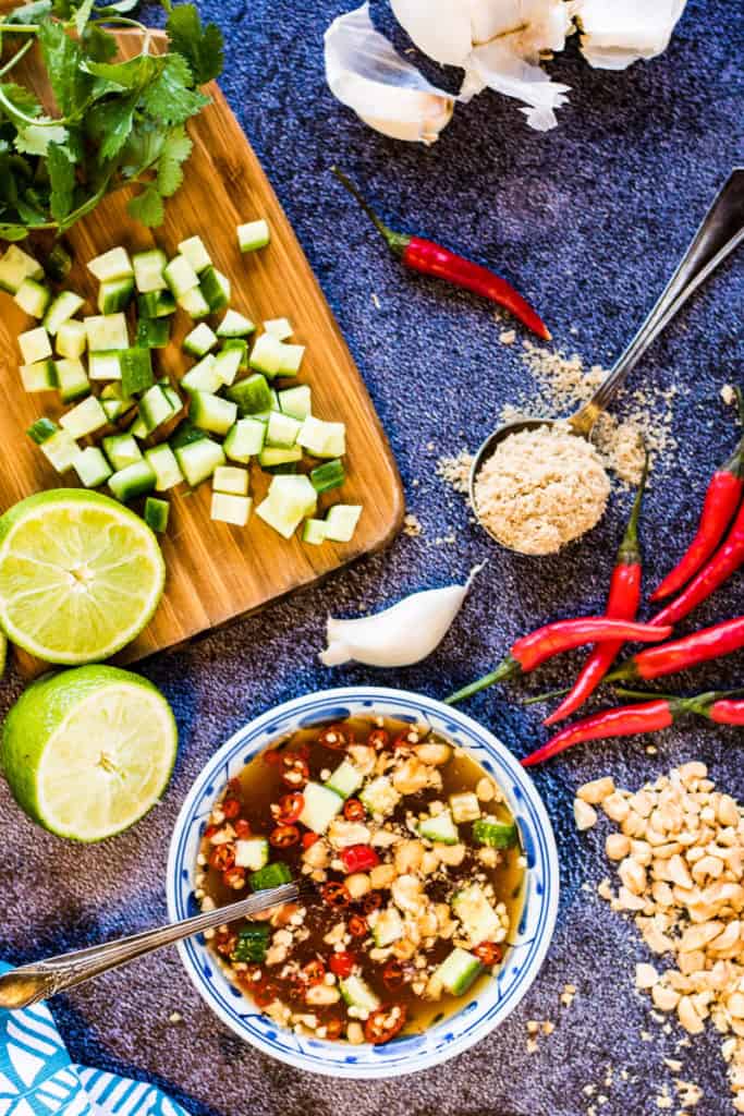 overhead shot of a bowl of prik nam pla with cut limes, chilies, crushed peanuts, sugar, and garlic