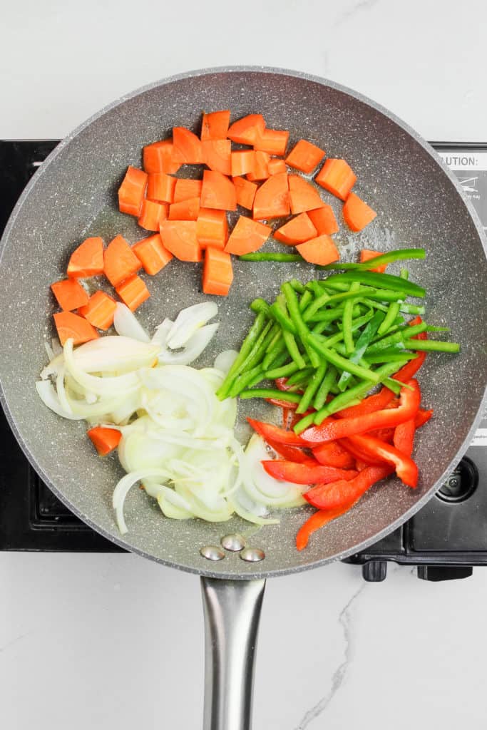 carrots, red and green bell pepper slices, and onion slices in a skillet.