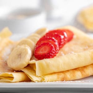 Low angle photo of folded crepes with sliced banana and strawberry on top.