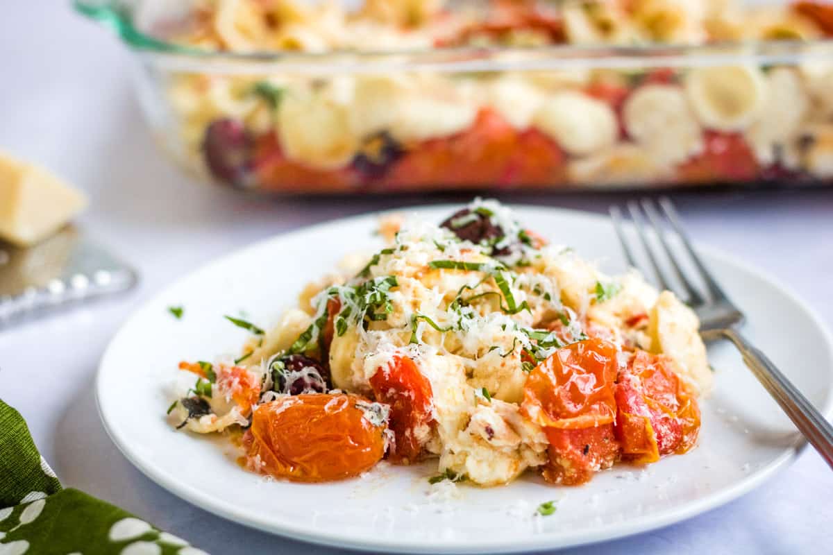 baked feta pasta on a white plate with a baking dish with the pasta in it in the background.