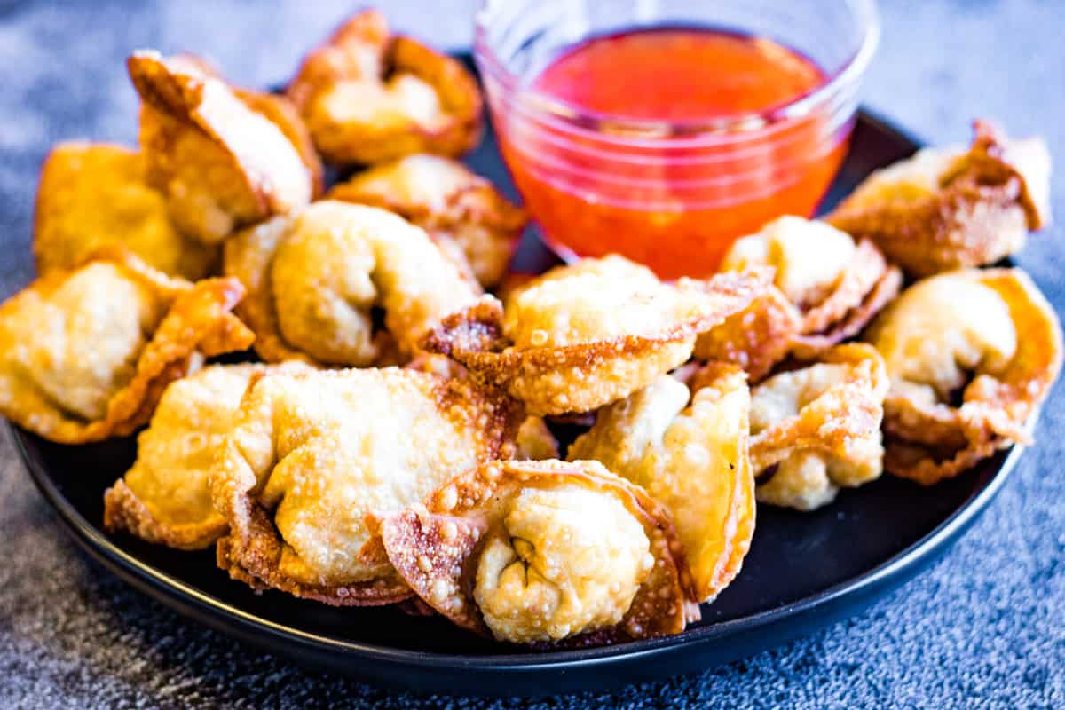 low angle shot of a plate of fried wontons with a bowl of sweet chili dipping sauce.