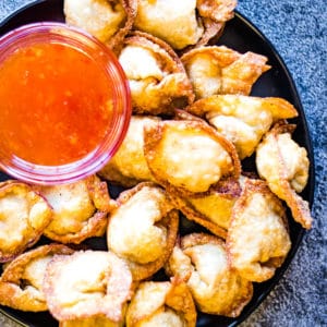 overhead shot of fried wontons on a plate with a bowl of sweet chili dipping sauce.