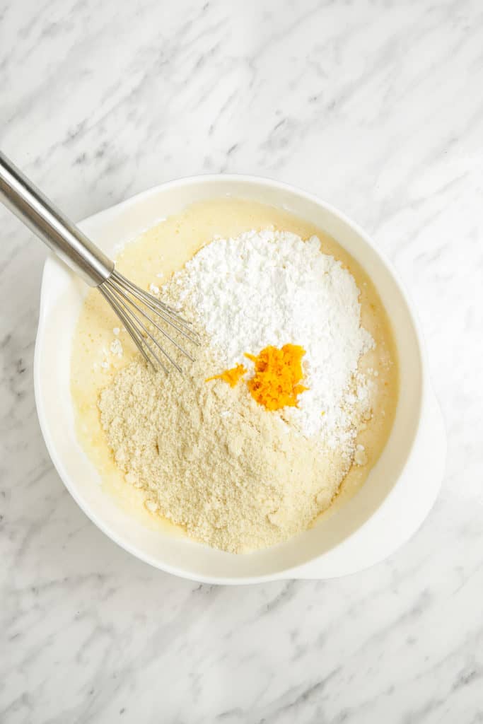 A passover sponge cake topped with a white bowl filled sugar and orange zest.