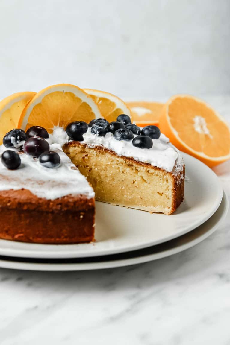Low angle shot of the whole cake minus one slice. The cake as whipped cream, blueberries, and orange slices on top.