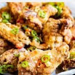A plate of crispy Chinese salt and pepper chicken wings, garnished with sliced green and red chili peppers, makes for a flavorful and aromatic appetizer.