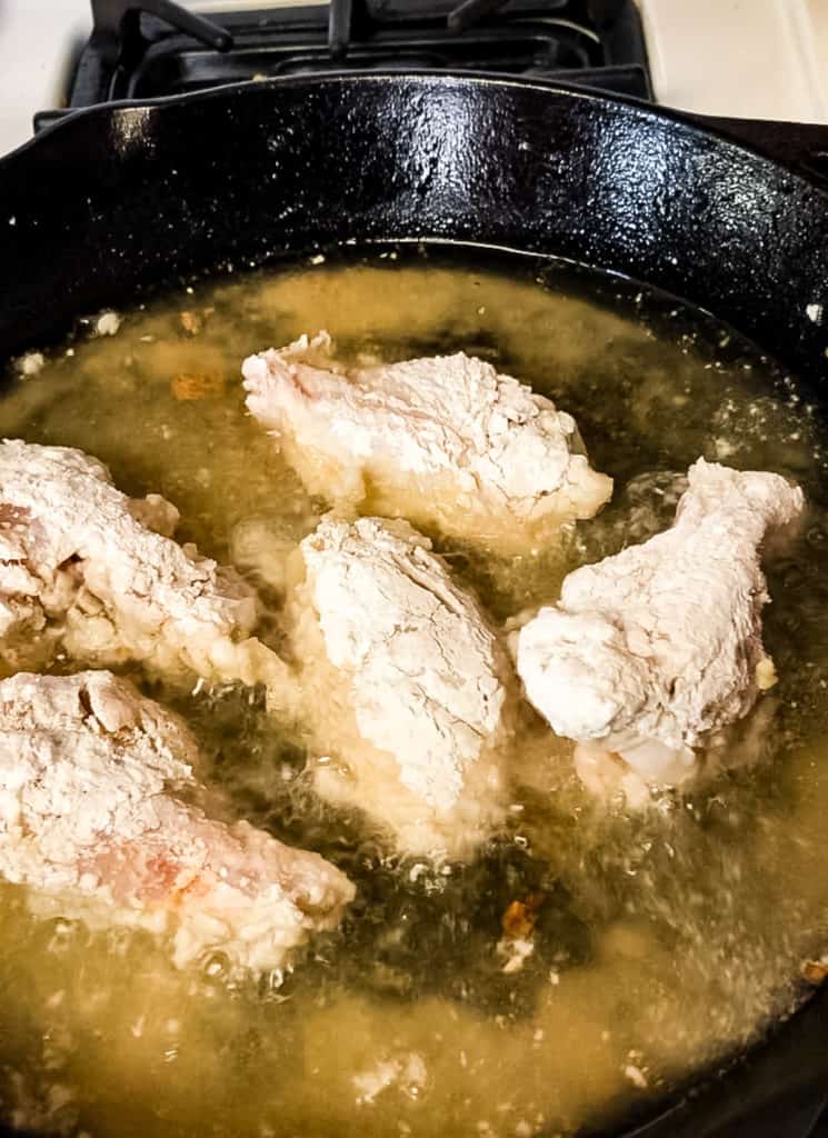 Low angle shot of the chicken being fried in oil in a cast-iron skillet.