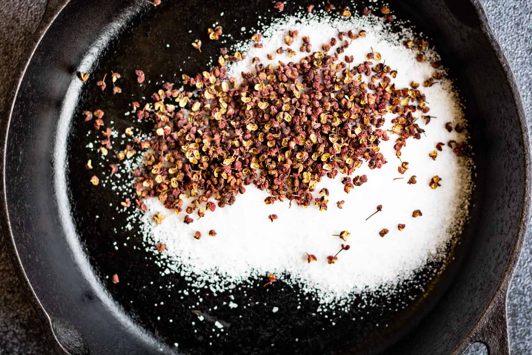 Overhead shot of Szechuan peppercorns and kosher salt in a cast-iron skillet.