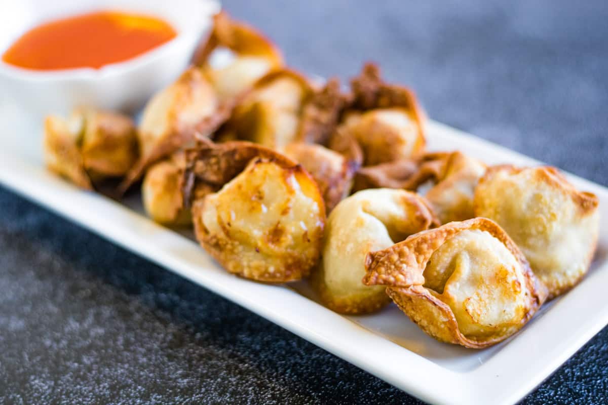 Low angle shot of air fryer wontons on a rectangular white plate with a small bowl of dipping sauce