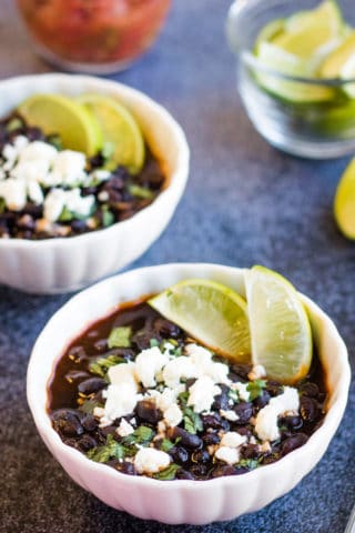 Low angle shot of two bowls of black beans garnished with cheese, cilantro, and lime juice.