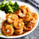 Low angle shot of Szechuan shrimp on a plate with steamed rice and broccoli.