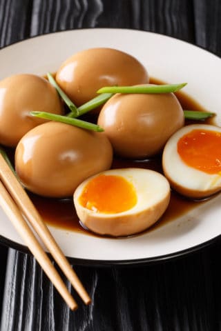 A low angle shot of soy sauce eggs on a white plate.