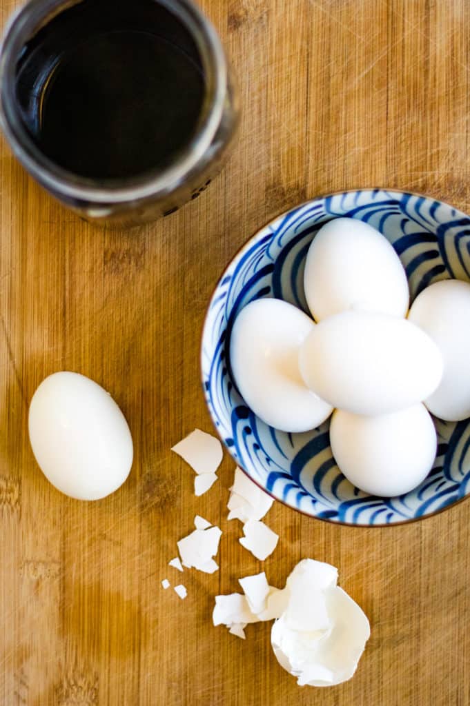 Hard boiled eggs in a bowl with a peeled egg on the side.