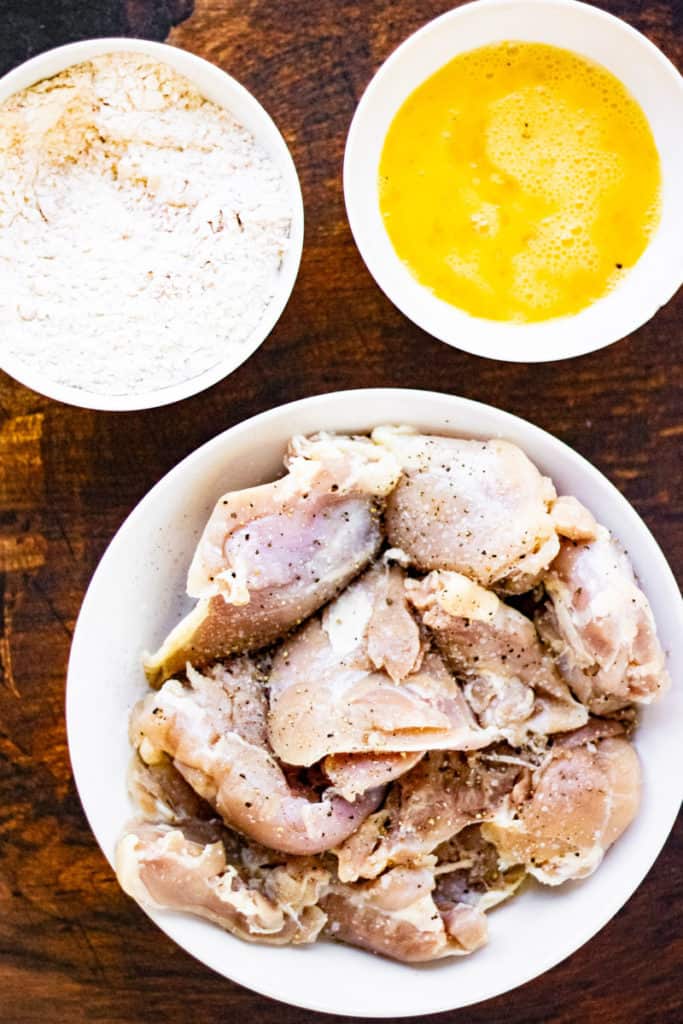 A wooden table displaying a bowl of flour-coated chicken, ready to be air fried.