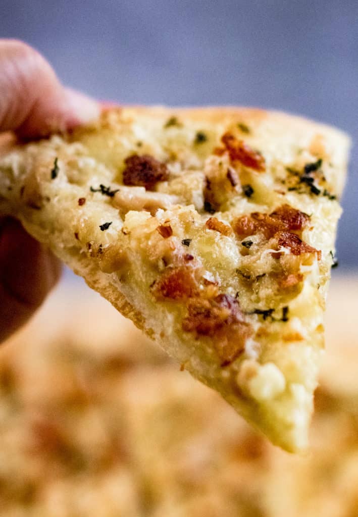 Close up of a slice of white clam pizza in someone's hand.
