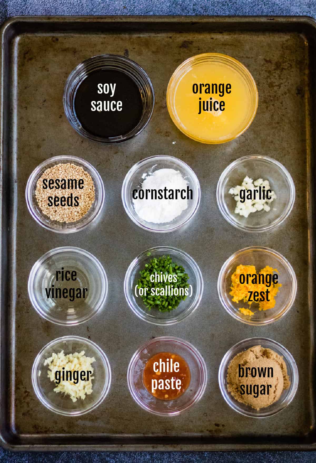 A baking sheet with various ingredients on it, including orange chicken.