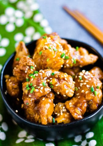 Low angle shot of air fryer orange chicken in a black bowl.