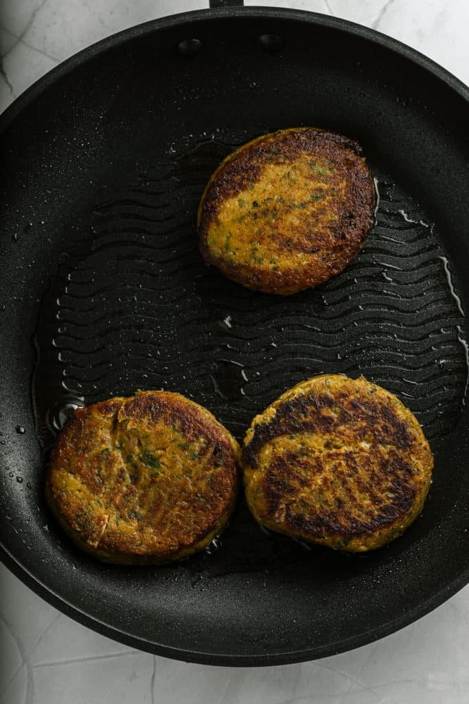 Three chickpea burgers are being fried in a pan.
