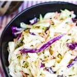 A black bowl filled with creamy coleslaw, garnished with shredded purple and green cabbage, and carrot slices. Text at the top reads "Best Creamy Coleslaw Recipe" and at the bottom "allwaysdelicious.com".