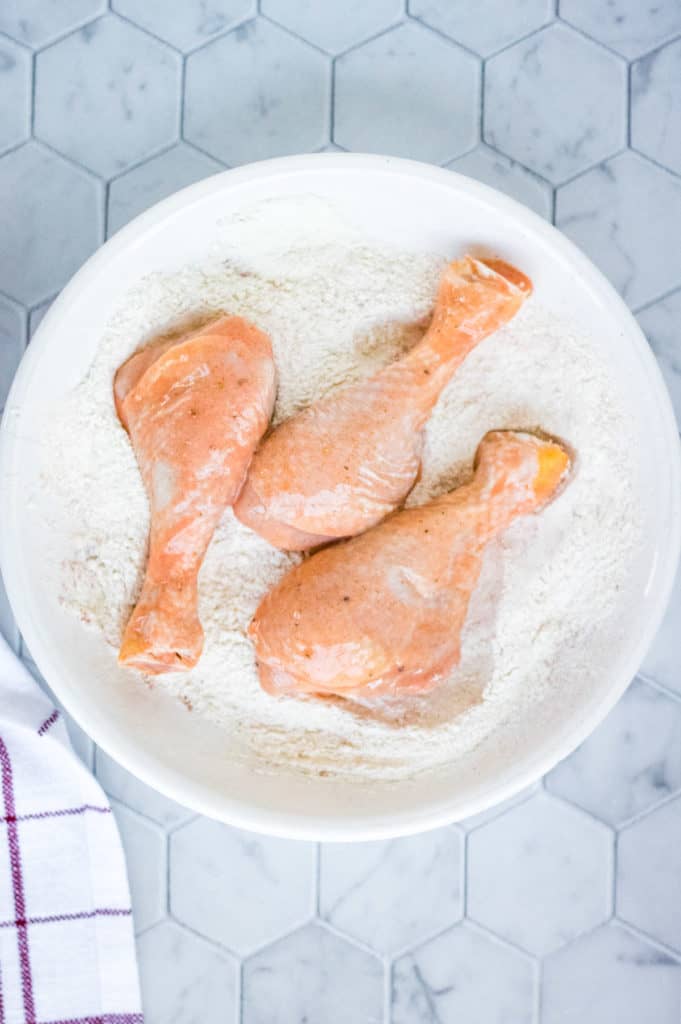 Air-fried chicken legs served in a white bowl on a marble counter.