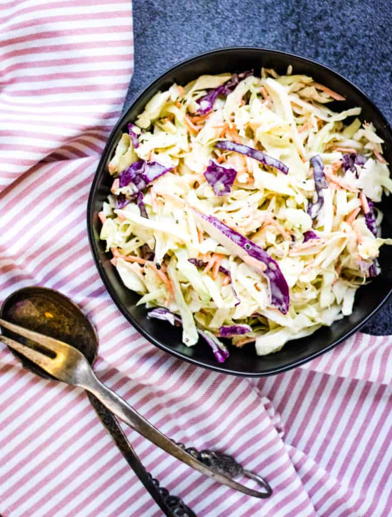 Coleslaw served in a bowl on a striped tablecloth.