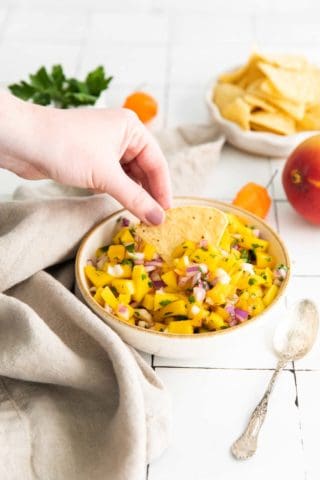 Low angle shot of mango salsa with a hand dipping a tortilla chip into the salsa.