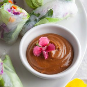 close up shot of a bowl of vietnamese peanut sauce with a bright pink edible flour on top.