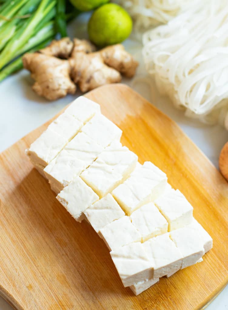 tofu cut into cubes on a wooden cutting board.