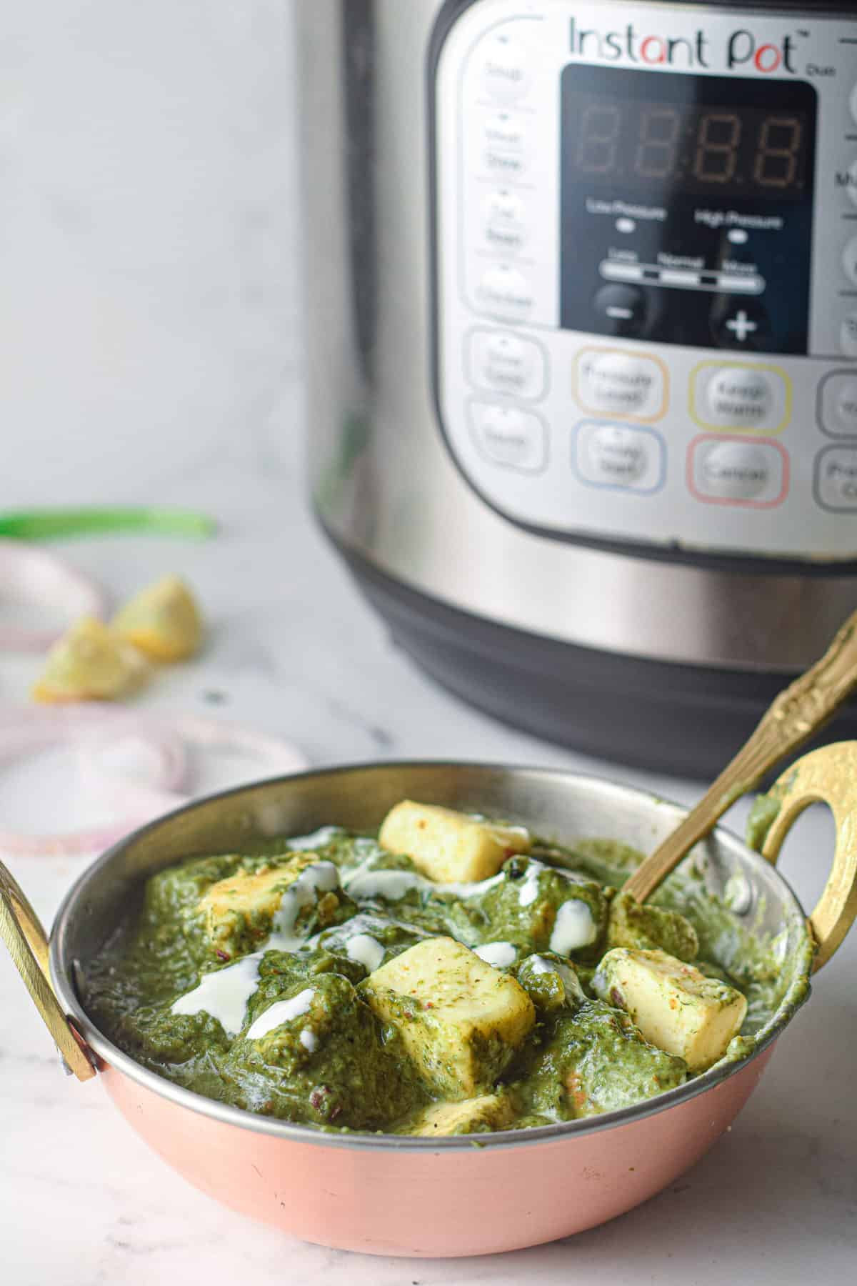 low angle shot of a bowl of palak paneer in front of an Instant Pot