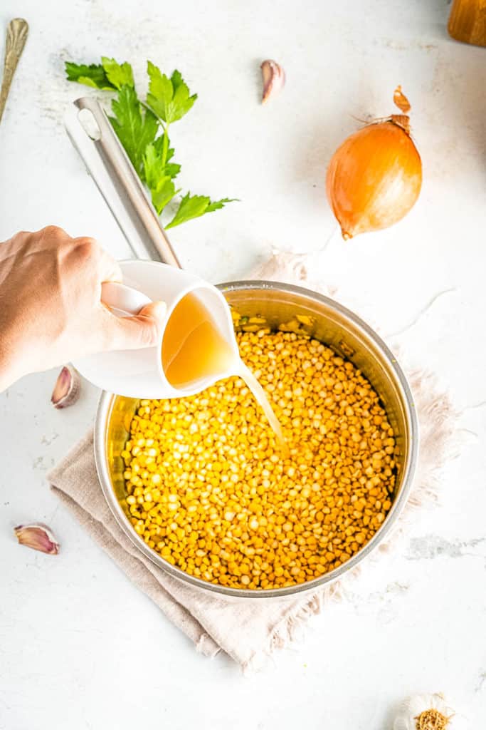 A person pouring oil into a pan of lentils.