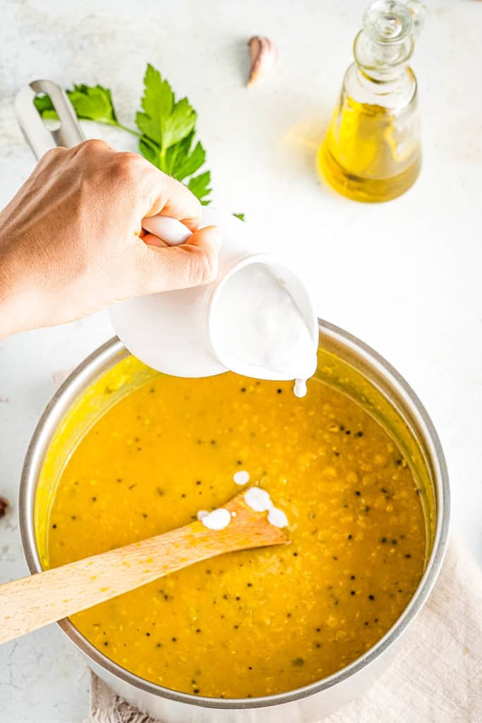 A person pouring olive oil into a bowl of soup.