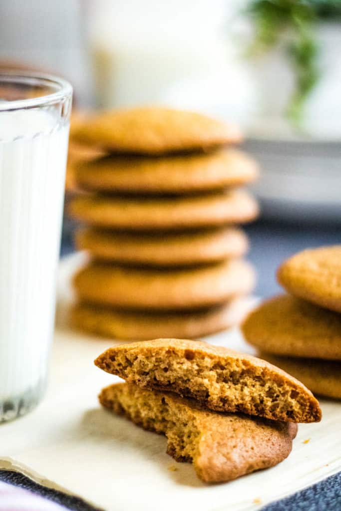 low-angled shot of a honey cookie broken in half with stacks of honey cookies and a glass of milk in the background