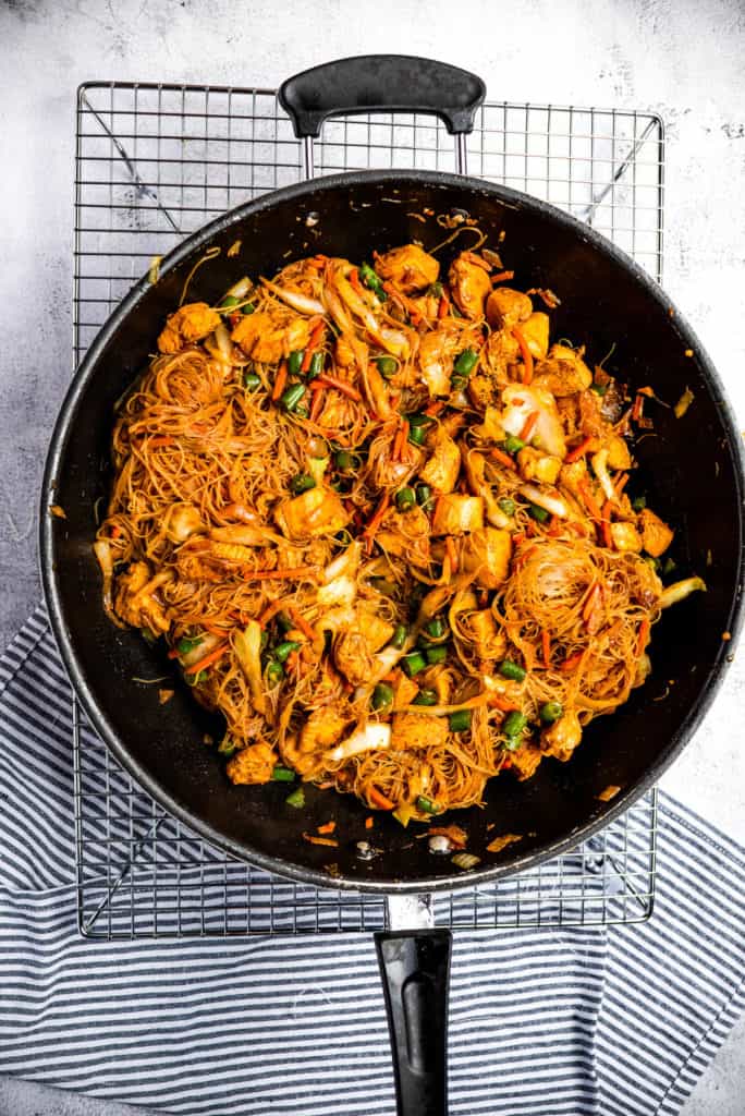 Chicken and vegetables stir-fried with pancit bihon noodles in a wok.