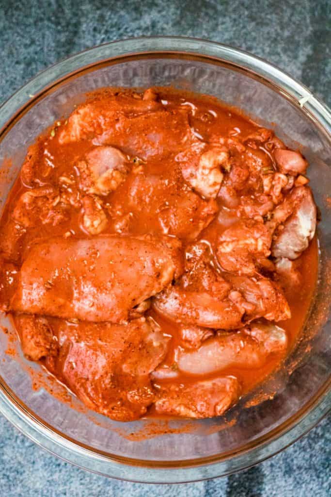 A glass bowl filled with pollo pibil in a red sauce.