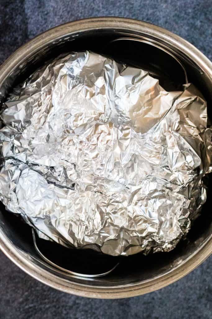 A bucket of foil containing pollo pibil sitting on a table.