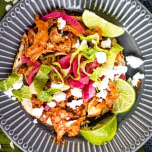 Overhead shot of pollo pibil on a corn tortilla with pickled onions, limes, lettuce, and cotija cheese