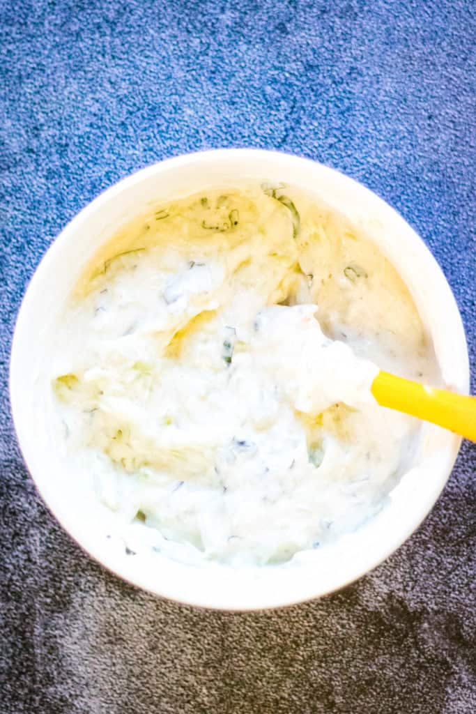 A bowl of cucumber raita with a yellow spoon.