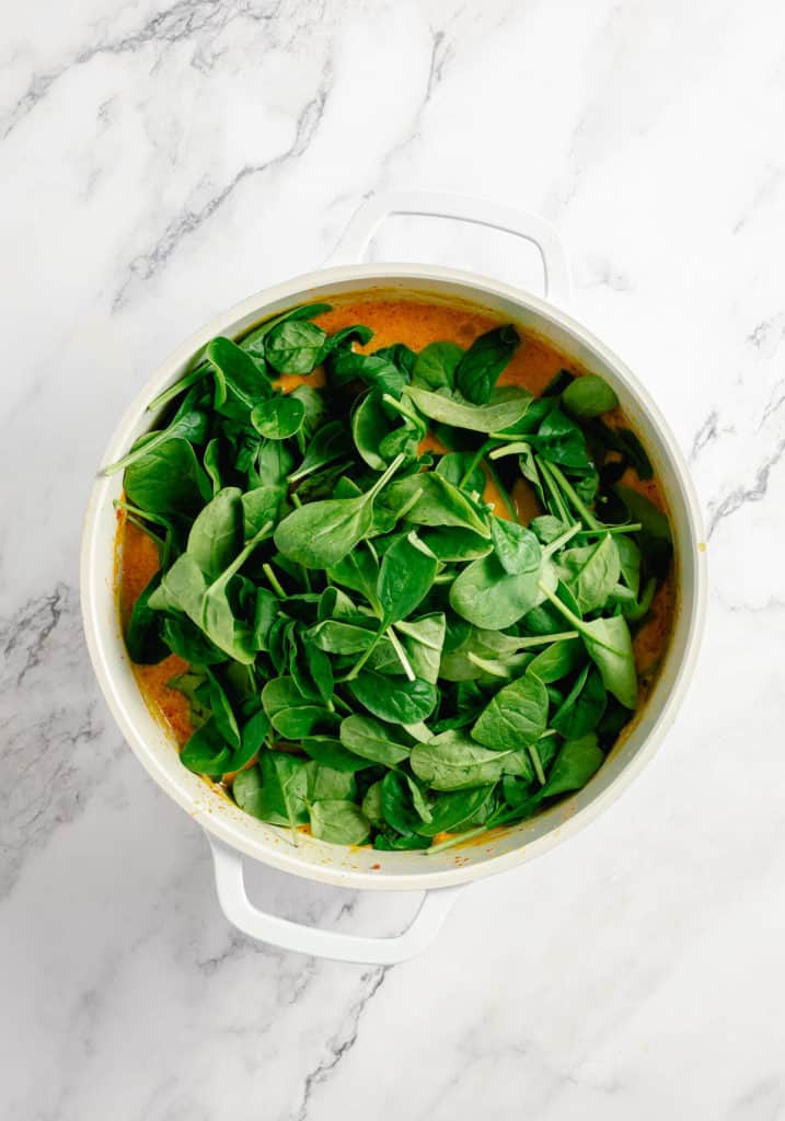 Spinach in a white bowl on a marble countertop, alongside Thai pumpkin curry.