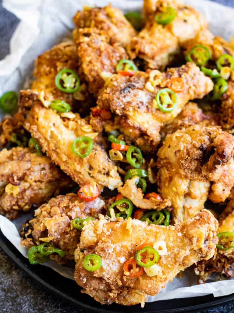 Fried chicken wings on a plate with green peppers.